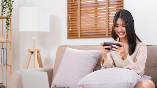 Lifestyle at home concept Jonge Aziatische vrouw gebruikt smartphone om games te spelen terwijl ze op de bank zit