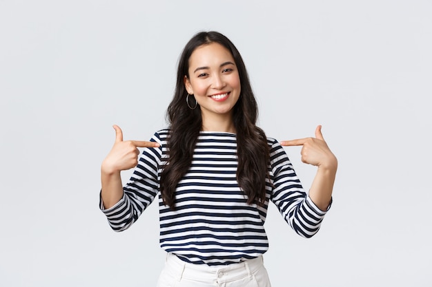 Lifestyle, beauty and fashion, people emotions concept. Smiling friendly-looking woman ready to help, pointing herself with pleasant look, bragging own accomplishments, whtie wall