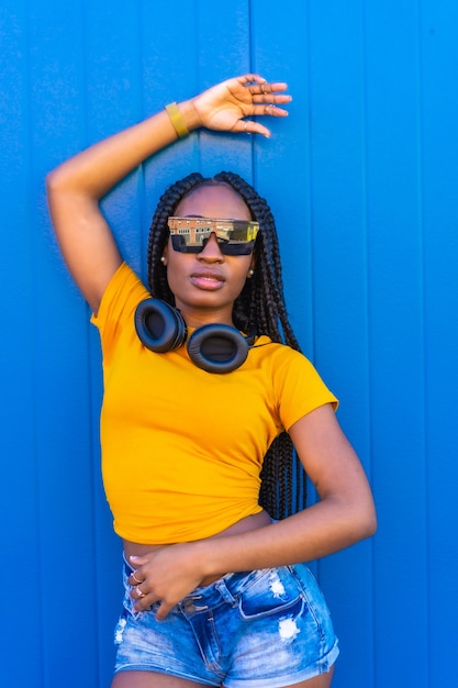 Lifestyle, black girl with long braids, in a yellow shirt and sunglasses. Dj with headphones smiling