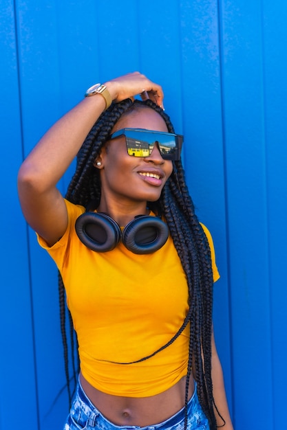 Lifestyle, black girl with long braids, in yellow t-shirt and sunglasses. Sexy girl and dj with headphones smiling