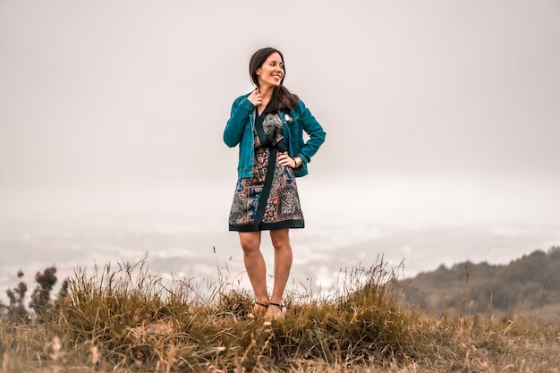 Lifestyle, brunette girl enjoying nature with colorful dress and a jacket on top of a mountain