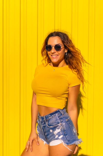 Lifestyle, Caucasian blonde girl in yellow t-shirts and short jeans on a yellow wall. Fashionable posing with a smile