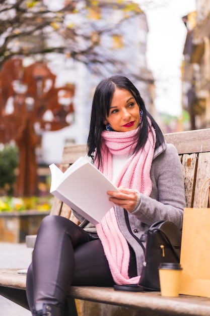 Stile di vita, ragazza bruna caucasica leggendo un libro in un parco, sorridente seduto su una panchina