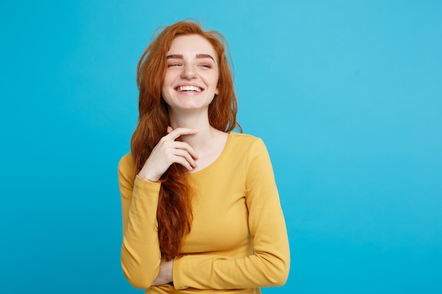 Concetto di stile di vita - close up ritratto di giovane bella ragazza attraente di zenzero rosso capelli che giocano con i capelli con timidezza. sfondo blu pastello. copia spazio.