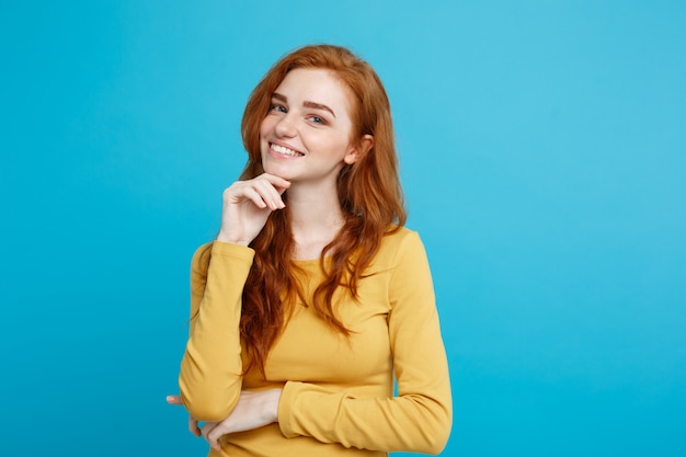 Concetto di stile di vita - close up ritratto di giovane bella ragazza attraente di zenzero rosso capelli che giocano con i capelli con timidezza. sfondo blu pastello. copia spazio.