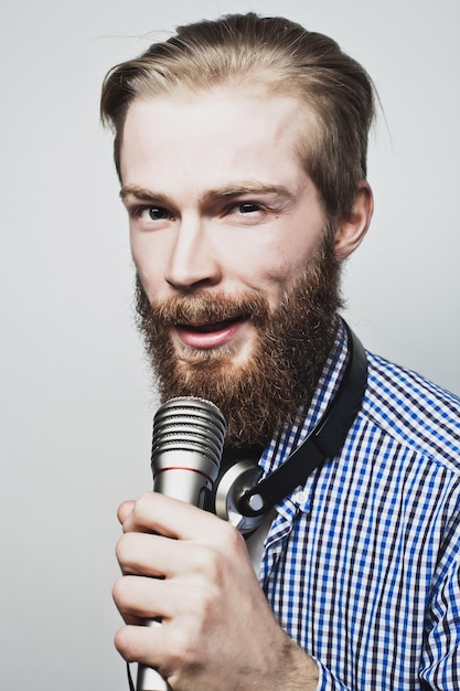 Lifestyle concept een jonge man met een baard die een wit shirt draagt met een microfoon en zingt op een grijze achtergrond
