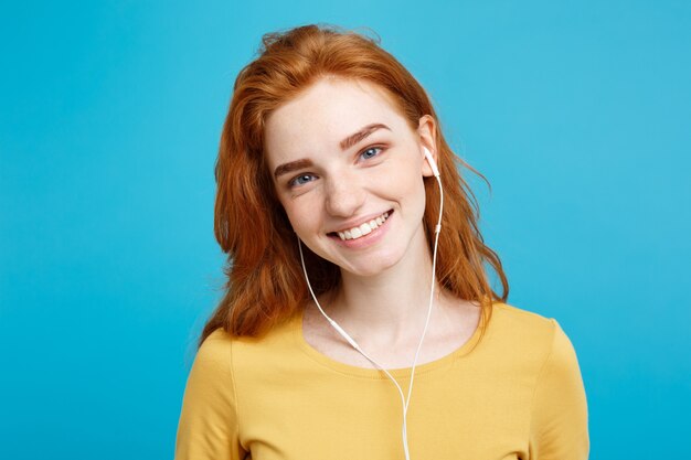 Lifestyle concept  portrait of cheerful happy ginger red hair girl enjoy listening to music with headphones joyful smiling  isolated on blue pastel wall copy space