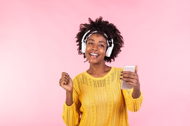 Lifestyle Concept Portret van een mooie Afro-Amerikaanse vrouw die vrolijk naar muziek luistert op haar mobiele telefoon trendy stijlvol schattig meisje met koptelefoon die naar muziek luisterd en danst op een geïsoleerde roze achtergrond