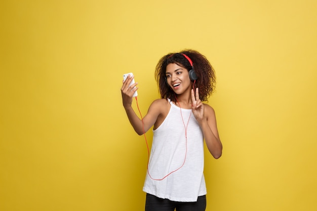 Lifestyle Concept - Portret van mooie Afrikaanse Amerikaanse vrouw blij muziek aan de mobiele telefoon te luisteren. Gele pastel studio achtergrond. Ruimte kopiëren.
