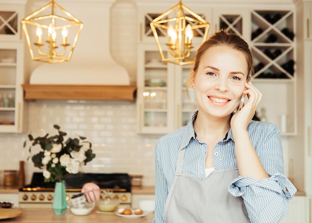 ライフスタイルの料理とフリーランスのコンセプト、台所で料理をしながら携帯電話で話す若い幸せな女性