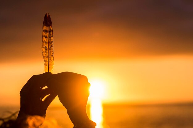 Lifestyle and dreaming hope concept image close up of hands\
holding leaf against a colorful amazing sunset on the ocean freedom\
and summer holiday travel vacation people life positive