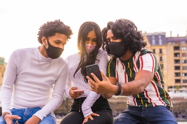 Lifestyle, drie vrienden kijken naar sociale netwerken op straat met gezichtsmaskers.
