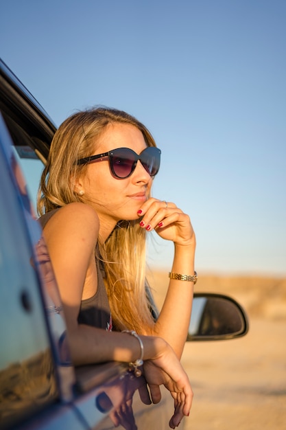 Lifestyle, een jonge blonde blanke vrouw met zonnebril in een auto in de woestijn van Bardenas Reales, Navarra. Spanje