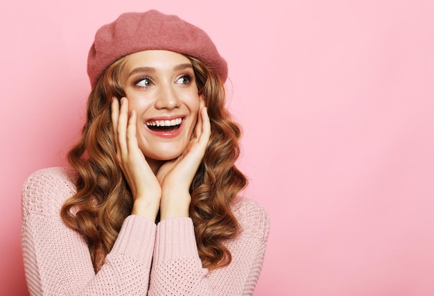 Lifestyle emotion and people concept Beautiful young surprised woman wearing pink shirt and beret over pink background