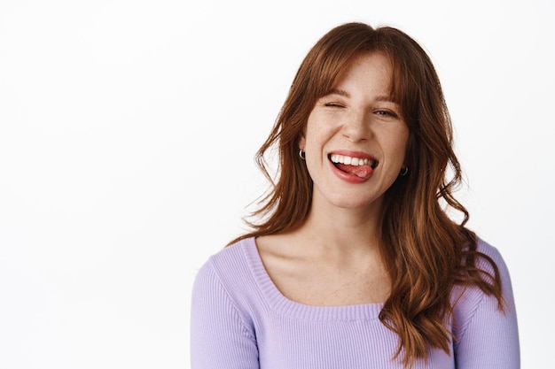 Stile di vita ed emozioni. felice ragazza positiva con le lentiggini, sorridente e mostrando la lingua, divertendosi, godendosi l'estate, in piedi in camicetta su sfondo bianco.