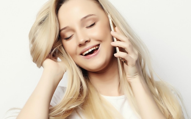 Lifestyle en mensen concept Mooie gelukkige blonde vrouw praat aan de telefoon en raakt haar haar aan