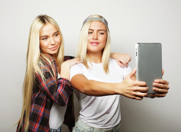 Lifestyle en mensen concept twee hipster meisjes vrienden nemen selfie met digitale tablet studio opname over grijze achtergrond