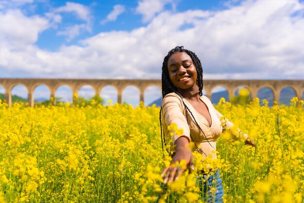 Lifestyle enjoying nature in freedom portrait of a black ethnic girl with braids in a field of yellow flowers