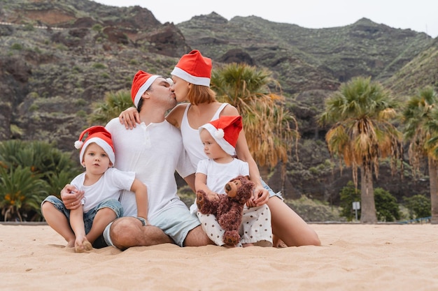 Photo lifestyle family portrait on ocean beach in christmas santa claus red hats caps christmas or new year vacation and holidays family with kids spending time together outdoors