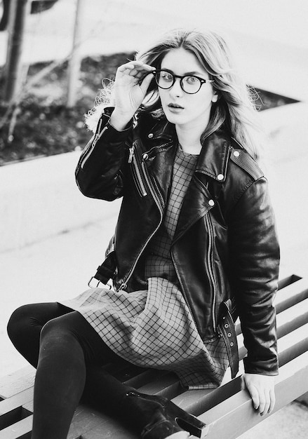 Lifestyle fashion and people concept blonde gir sits on a bench summer city black and white picture