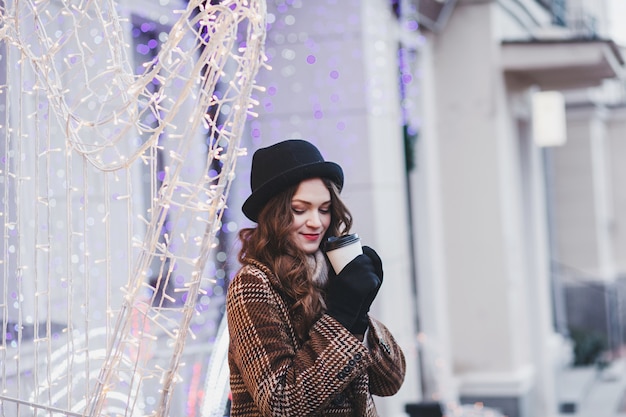 Lifestyle fashion portrait of stunning girl.  Wearing stylish coat and drinking coffee in city