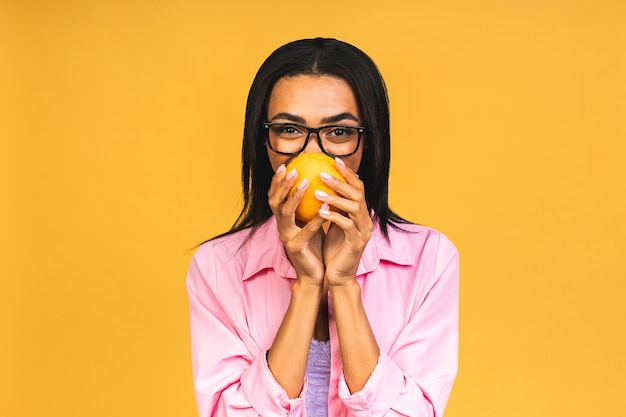 Lifestyle food diet and people concept photo of young cheerful african american woman holding orange fruit empty space isolated on yellow color background