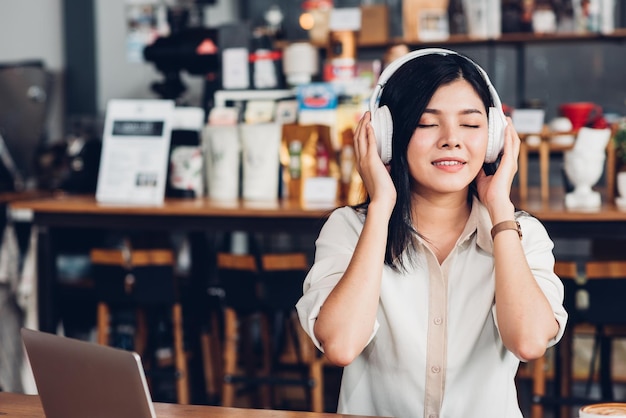 コーヒー ショップでラップトップ コンピューターで作業中に音楽を聴くイヤホンを使用してライフ スタイルのフリーランスの女性