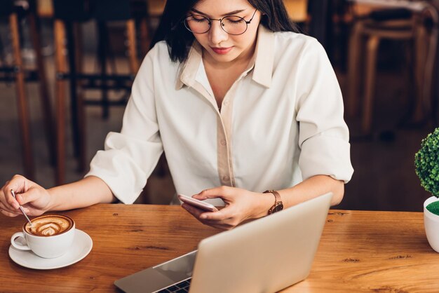 ライフ スタイル フリーランスの女性彼モバイル スマート フォンを使用して、コーヒー ショップでメディアをオンラインで社交