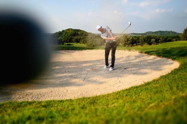 Lifestyle, golf, activity, outdoor, sport, golfer concept. A close-up golf ball blurred by man is sweeping golf on the sand at a golf course in the summer. Sport lifestyle Concept. Bright picture.