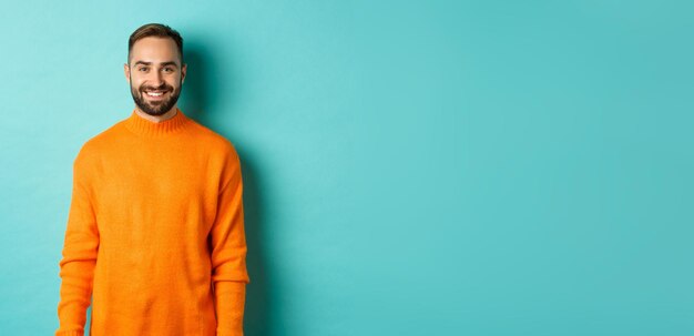 Photo lifestyle handsome man in orange sweater smiling at camera happy face guy cheerful expression standi