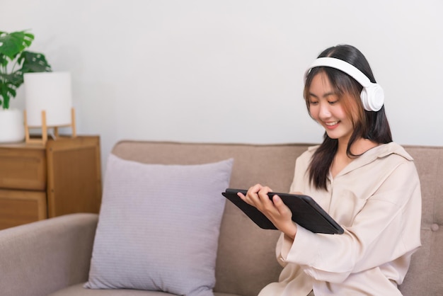 Lifestyle at home concept Young Asian woman is listening music and surfing social media on tablet