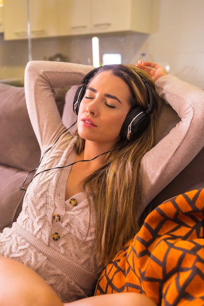 Lifestyle at home, young Caucasian woman listening to music with headphones on the sofa at home