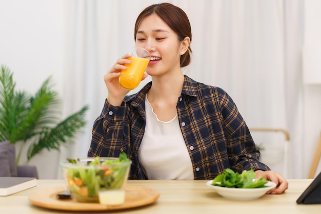 Lifestyle in woonkamer concept Aziatische vrouw die sinaasappelsap drinkt en groentesalade eet