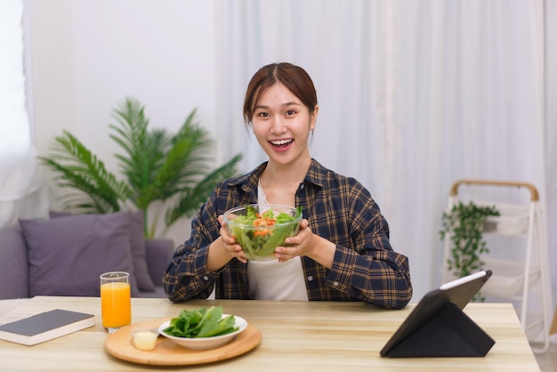 Lifestyle in woonkamer concept Jonge Aziatische vrouw opgewonden terwijl ze een kom groentesalade vasthoudt