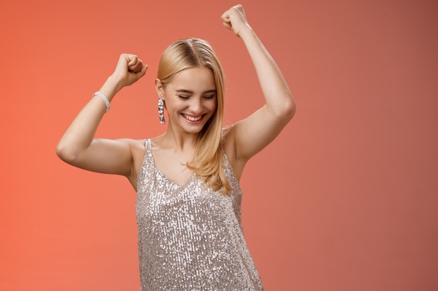 Lifestyle. joyful blond excited birthday girl having fun carefree dancing raised hands close eyes smiling enjoying night-out girlfriend nightclub have fun standing amused red background entertained.