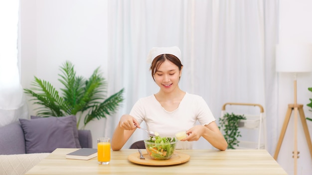 Lifestyle in living room concept Asian woman using spoon to ladle salad dressing into salad bowl