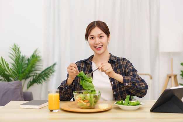 거실 개념의 라이프 스타일 태블릿을 보고 야채 샐러드를 먹는 젊은 아시아 여성