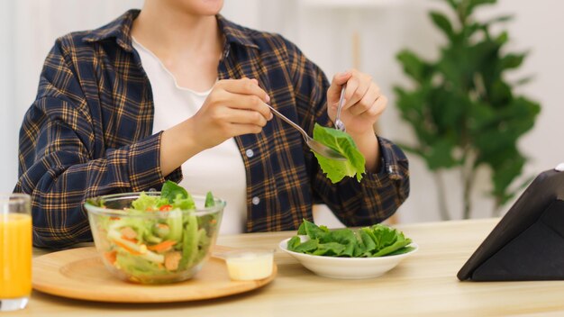 거실 개념의 라이프 스타일 태블릿을 보고 야채 샐러드를 먹는 젊은 아시아 여성