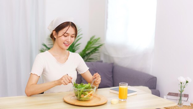 Photo lifestyle in living room concept young asian woman mixing vegetable salad in bowl for breakfast