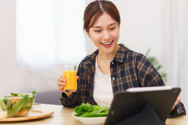 거실 개념의 라이프 스타일 태블릿을 가리키고 오렌지 주스를 마시는 젊은 아시아 여성