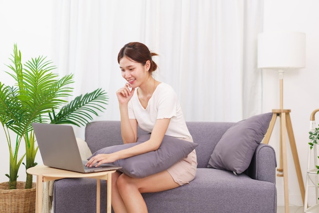 Lifestyle in living room concept Young Asian woman sitting with hand on chin and using laptop