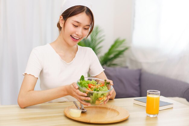 Photo lifestyle in living room concept young asian woman smiling and holding bowl of vegetable salad