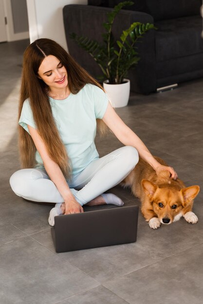 Lifestyle meisje en Corgi-hond Meisje met laptop die haar Welsh Corgi Pembroke-hond thuis aait Drukke jonge vrouw heeft een pauze en ontspan met haar hond Lifestyle met huisdier