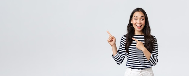 Lifestyle mensen emoties en casual concept Knappe jonge Koreaanse vrouw adverteren product lachende camera opgewonden en wijzende vingers linker bovenhoek op promo banner