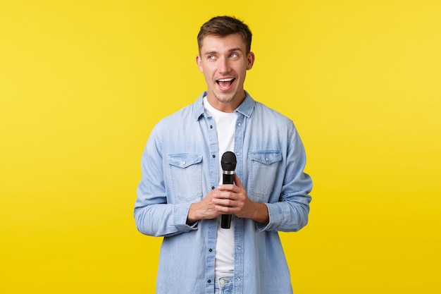 Lifestyle, mensen emoties en zomer vrije tijd concept. Enthousiaste gelukkige knappe blonde man die wegkijkt en glimlacht, op het podium praat, stand-up uitvoert of karaoke zingt met microfoon