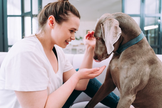 Lifestyle-momenten van een jonge vrouw thuis. Vrouw speelt met haar hond in de woonkamer