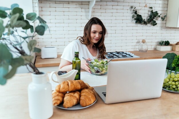 自宅で若い女性のライフスタイルの瞬間。キッチンでサラダを準備する女性