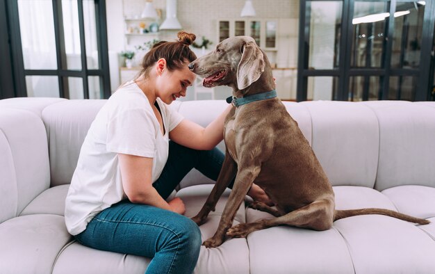 自宅で若い女性のライフスタイルの瞬間。居間で犬と遊ぶ女性