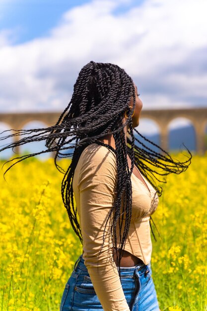 Lifestyle moving hair portrait of black ethnic girl with braids traveler in a field of yellow flowers