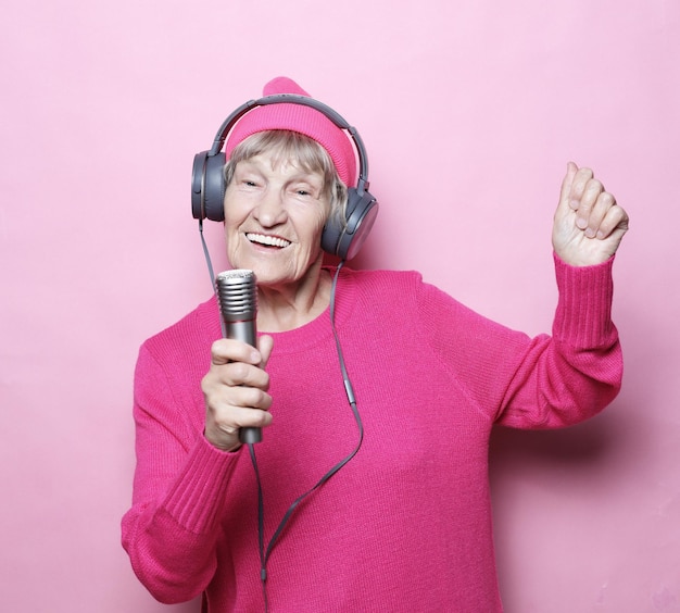 Lifestyle and people concept Funny old lady listening music with headphones and singing with mic